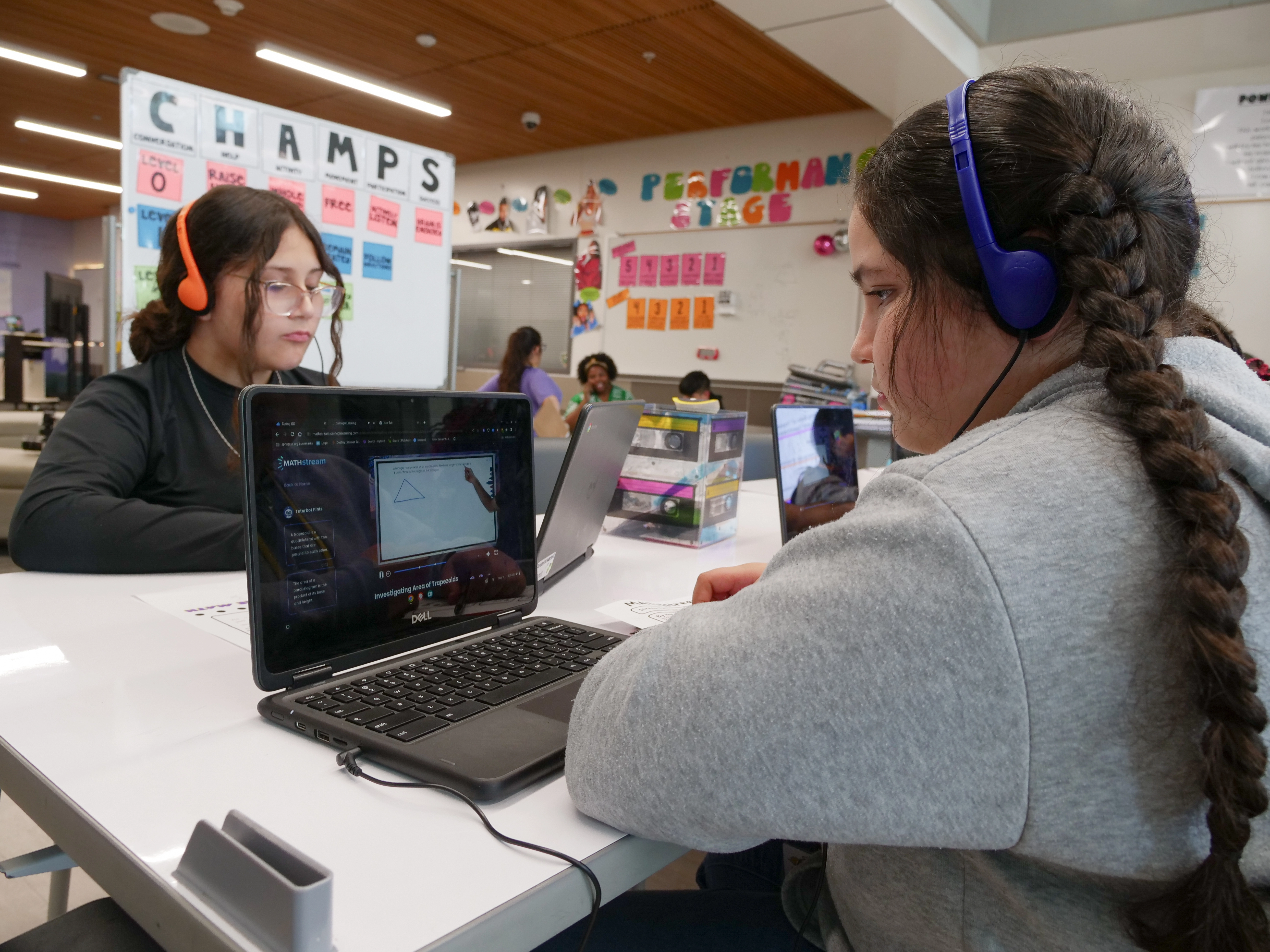 Two students seating across each other, wearing headphones and working with MATHstream on their computers. 