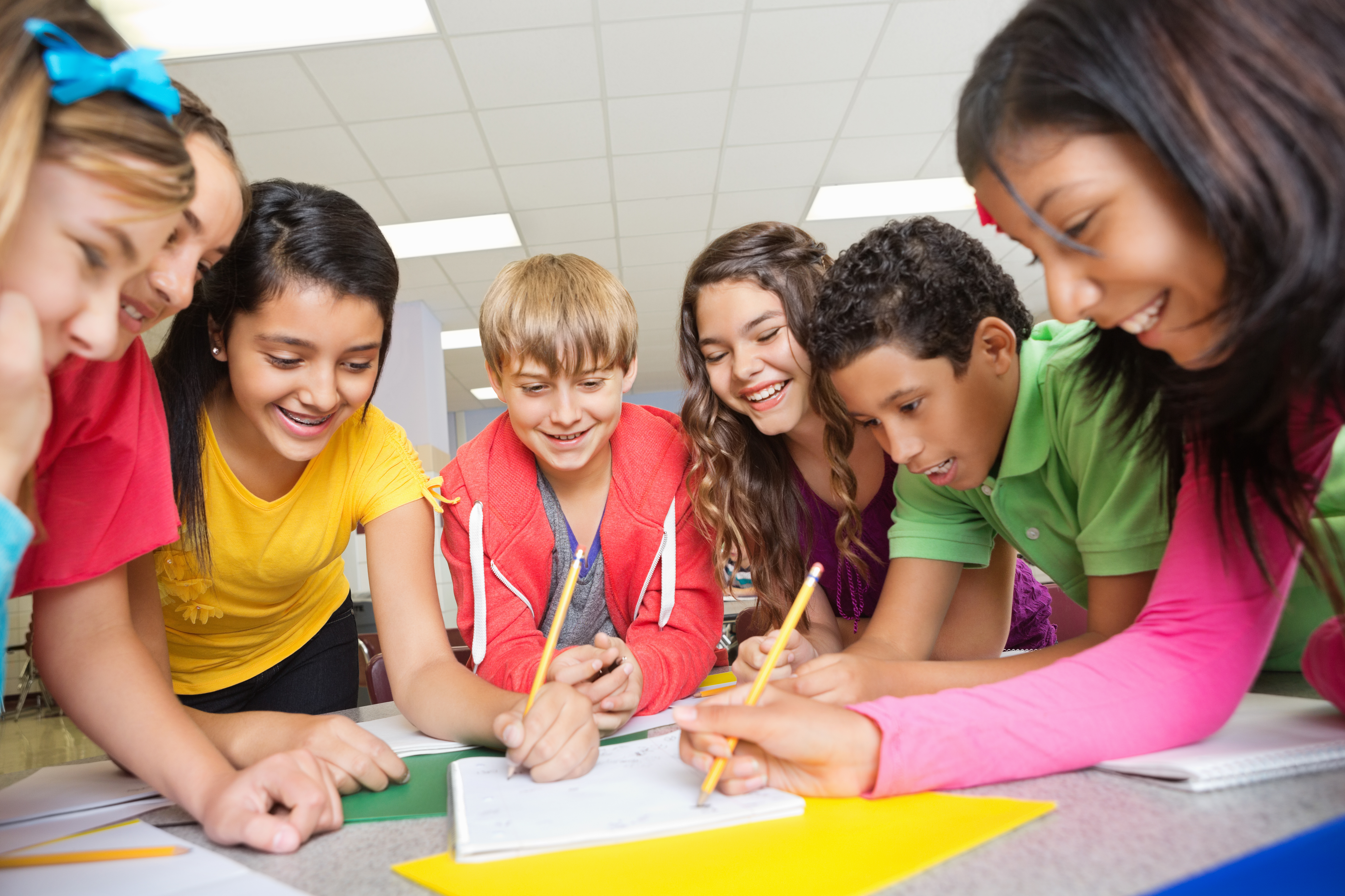 A group of middle school students collaborating and smiling in classroom for blog about playful learning tools