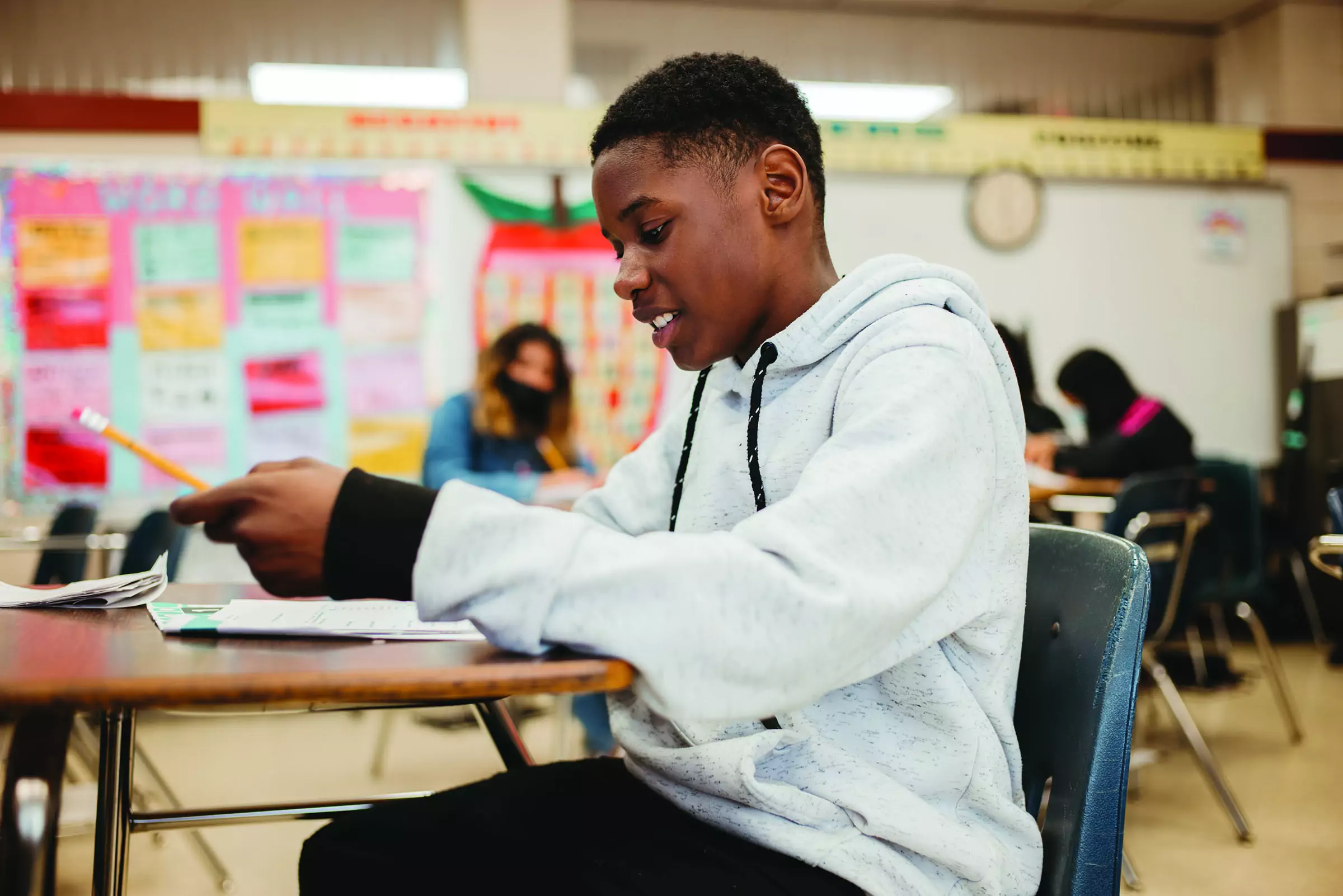 A middle school boy is sitting at a desk and smiling as he completes an SEL activity