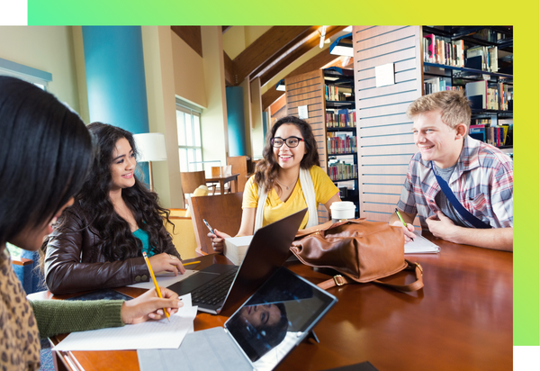 A group of students are sitting at a table together, with books, pencils, papers, and computers. They are collaborating.