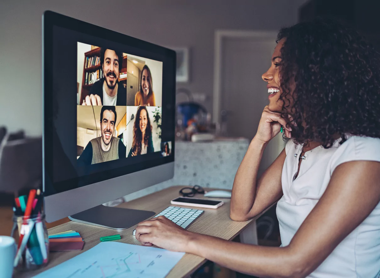 Woman sitting in front of computer. The computer shows four people, as a meeting.