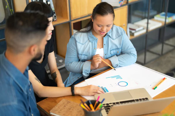 Three high school students sit together at a desk to build conceptual understanding in math. They are looking at graphs and visual representations.