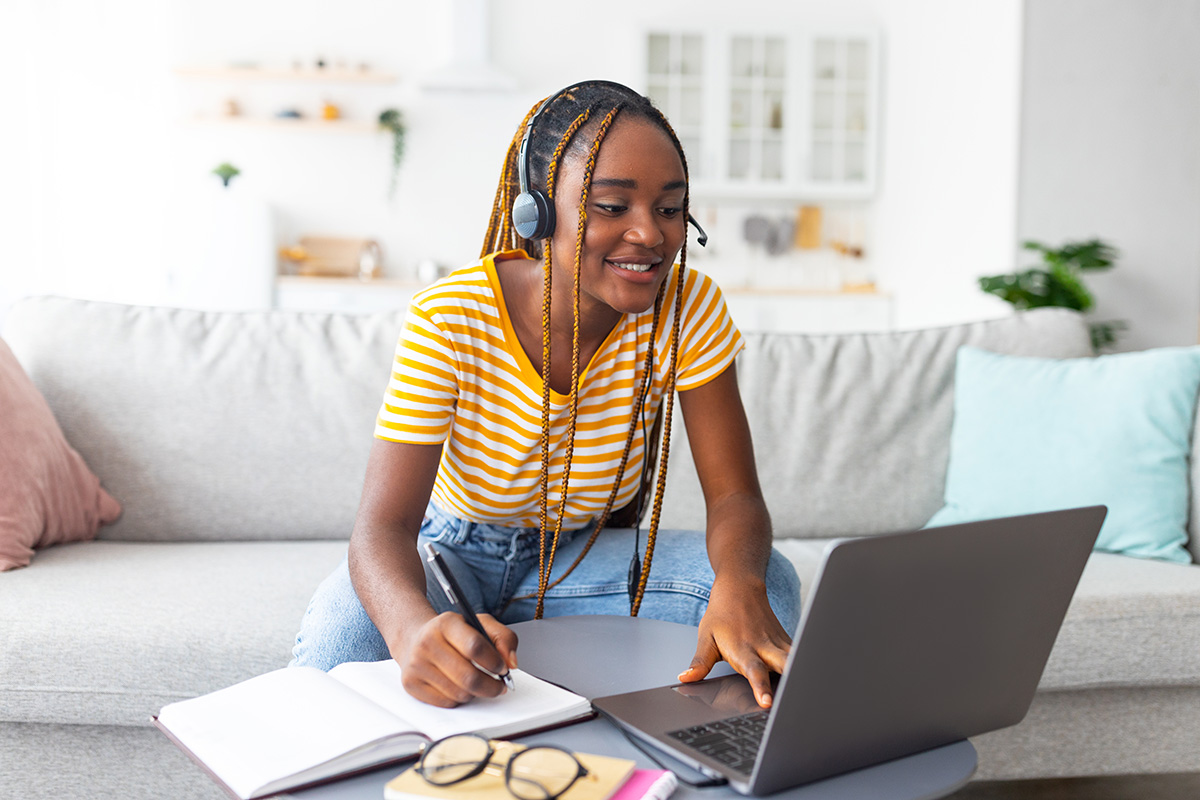 teen girl studying with a laptop, notebook, and headset